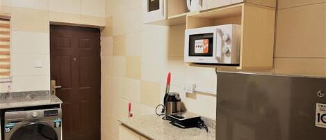 A compact kitchen with a washing machine, microwave, and refrigerator.