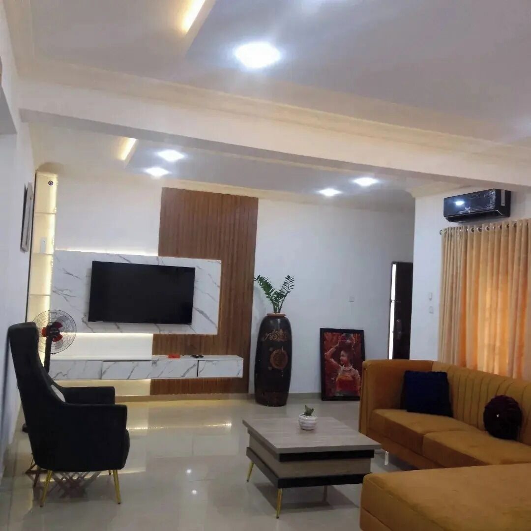 A modern living room with a flat-screen TV mounted on a marble wall, a black armchair, a yellow sofa, and a coffee table.