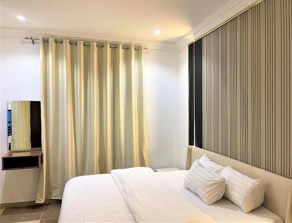 A hotel room with a bed, a bedside table, a mirror, and a curtain.