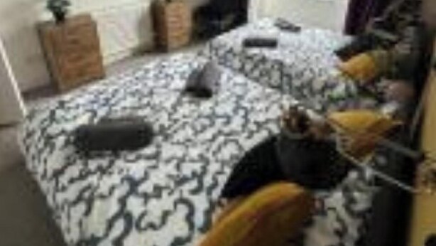 Un dormitorio con una colcha estampada, un escritorio, una silla y una ventana con cortinas.