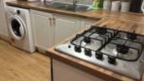 Una cocina con armarios blancos, estufa a gas, lavadora y salpicadero de azulejos.