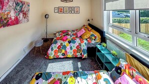 Un dormitorio con dos camas, un ventanal grande, un radiador y una pequeña mesa con plantas.