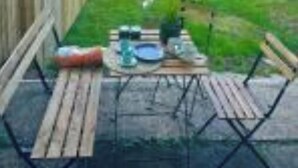 Terraza de madera con mesa lista para comer, rodeada de un cerco de madera y abundante follaje.