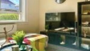 Una sala de estar con un sofá, una mesita, un televisor y una ventana que da a una vista de una casa.