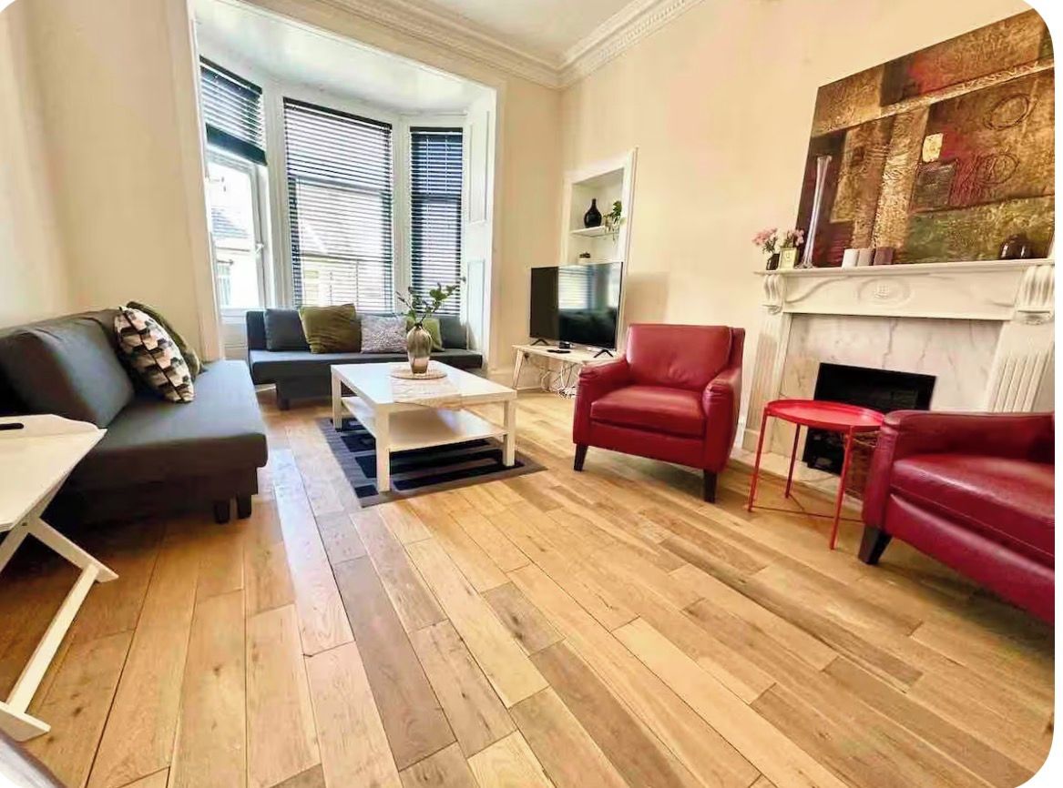 Ein Wohnzimmer mit einer Couch, Sesseln, einem Couchtisch, einem Kamin und einem Fernseher.