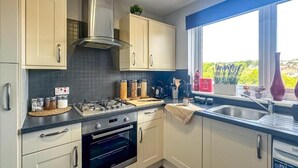 A modern kitchen with light-colored cabinets, a stainless steel range hood, a built-in oven, and a window with a view of greenery. - Brand New Scotland home 3rooms near Glasgow
 (Hardgate)