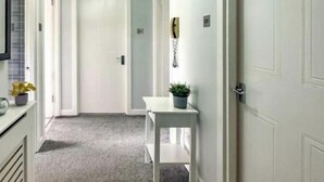 A hallway with a white door at the end, a small table with a plant, and a wall-mounted telephone. - Brand New Scotland home 3rooms near Glasgow
 (Hardgate)