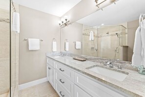 A modern bathroom with a large mirror, two sinks, and a shower area.