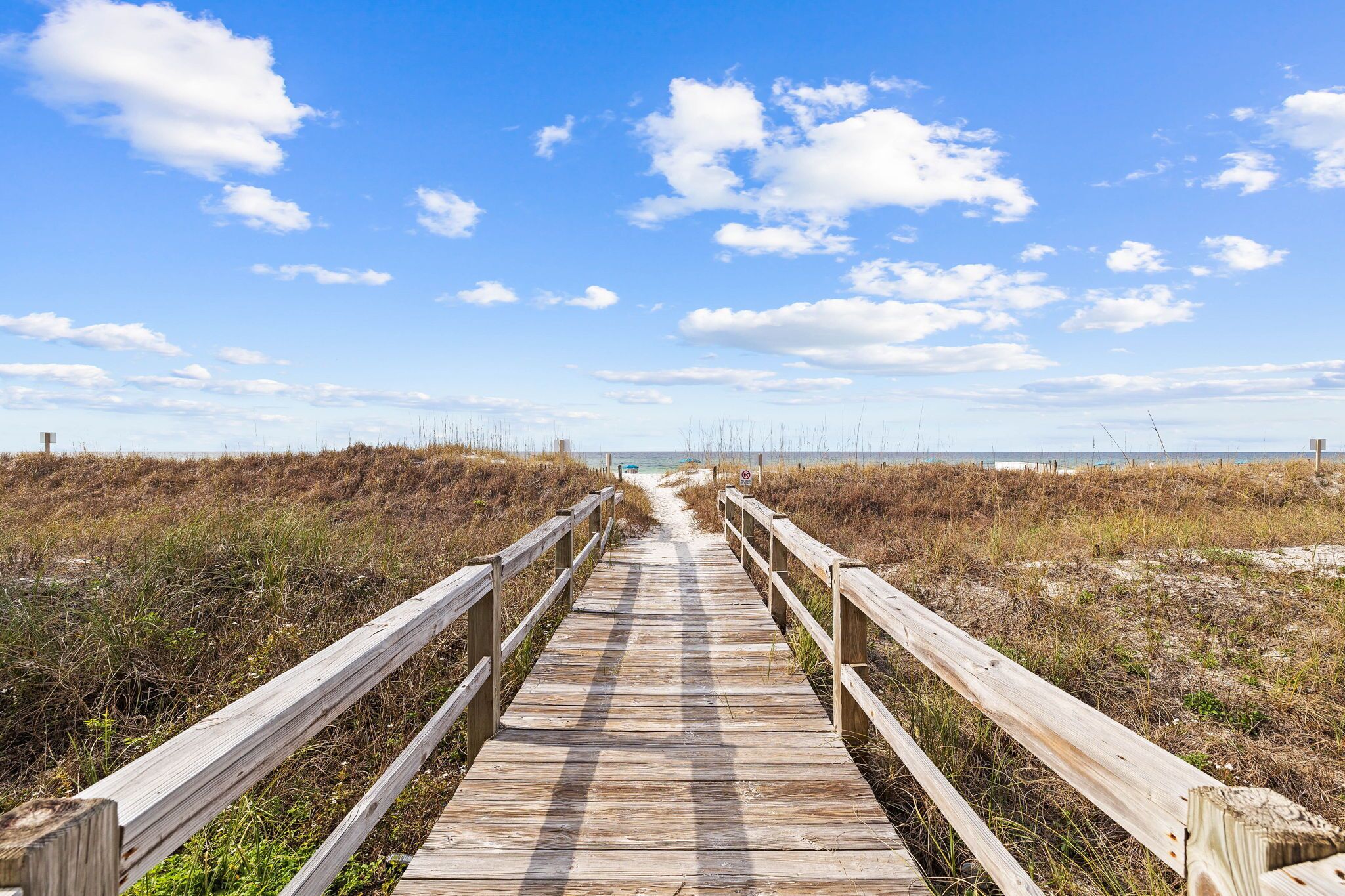 A wooden boardwalk leading to a beach with a clear sky.