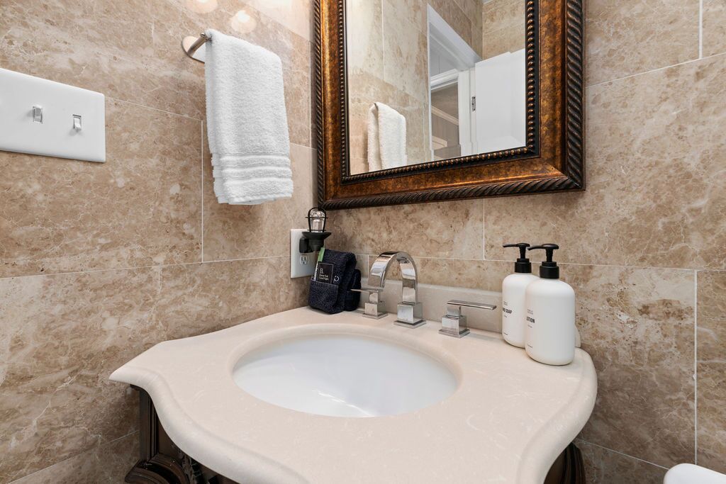 Une salle de bain avec un lavabo en marbre, un miroir avec un cadre en bois et des articles de toilette posés sur le comptoir.
