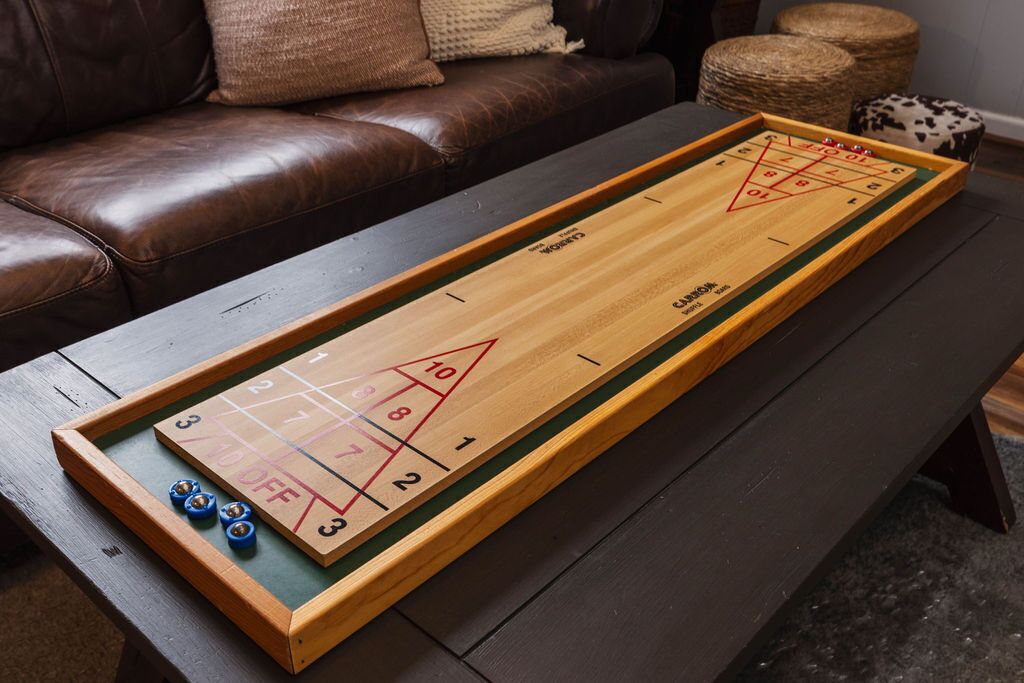 A shuffleboard table with a wooden frame, green felt surface, and numbered scoring areas.