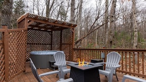 Een terras buiten met een jacuzzi, twee Adirondack-stoelen en een vuurplaats.