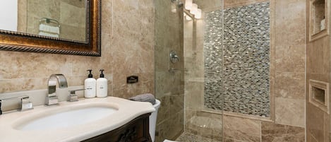 Un baño con lavamanos de mármol, cabina de ducha de vidrio y pared de ducha con mosaicos.