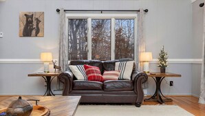 Een gezellige woonkamer met een leren bank, twee bijzettafeltjes met lampen, een kleine kerstboom en een kunstwerk met een beer thema aan de muur.