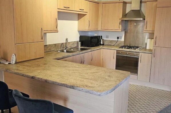 A kitchen with granite countertops, wooden cabinets, a gas stove, and a microwave.
