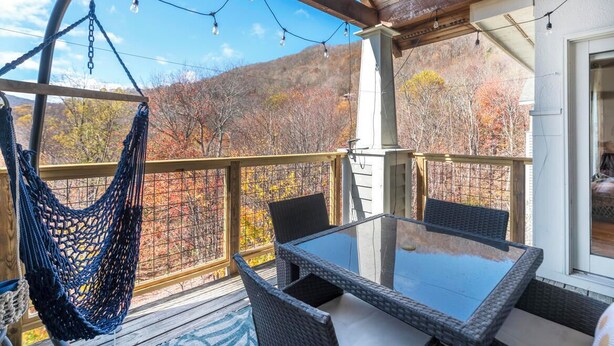 A covered outdoor area with a glass table and wicker chairs, a hammock, and a view of autumn trees. - Hawks Peak 406- Mtn Condo, Top Floor, Mtn View, Modern, Near Attractions (Seven Devils)