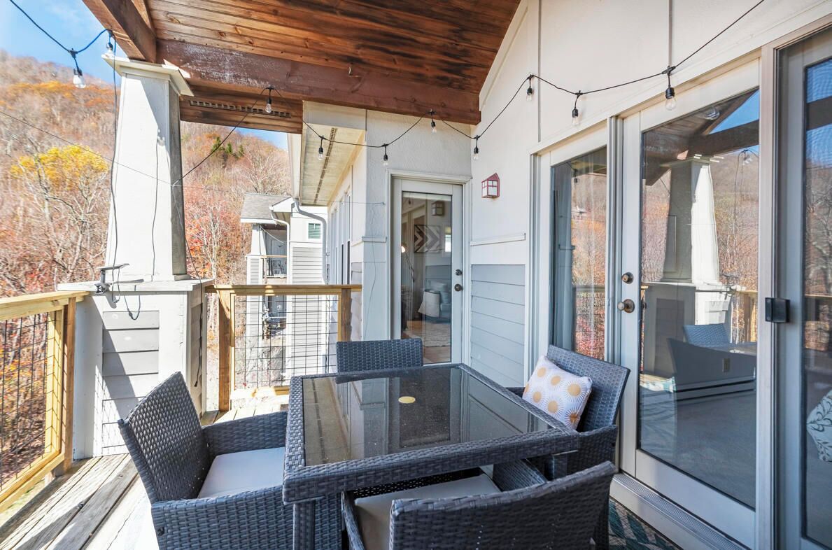 Eine überdachte Terrasse mit Glas-Tisch und Korbstühlen, ein Holzboden und Blick auf ein Haus und Bäume.