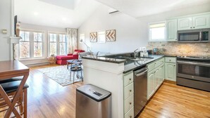 A spacious kitchen with a large island, a dining area with a red sofa, and a view of the outdoors through large windows. - Hawks Peak 406- Mtn Condo, Top Floor, Mtn View, Modern, Near Attractions (Seven Devils)