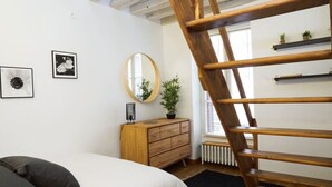 Ein Schlafzimmer mit einem Bett, einer Holzkommode, einem Spiegel und einer Treppe.