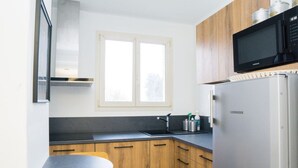 Moderni keittiö, jossa on puiset kaapit, ruostumattomasta teräksestä valmistettu jääkaappi, mikroaaltouuni ja ikkuna tiskialtaan yläpuolella.