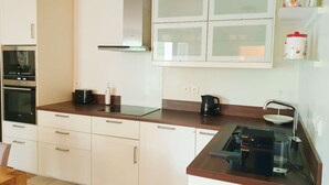 Eine moderne Küche mit weißen Schränken, einem Einbauofen, einer Kaffeemaschine und einem Wasserkocher.