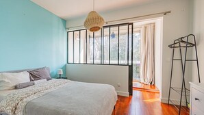 A bedroom with a bed, a bedside table, a hanging light, a window with curtains, and a ladder. - Beautiful flat 2 rooms near Paris/La Défense (Suresnes)
