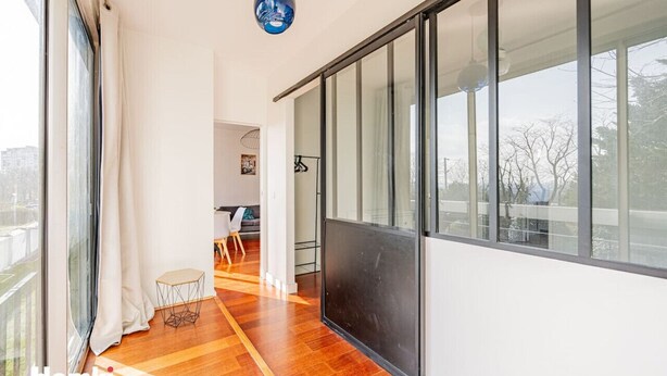A modern interior with a large sliding glass door, a wooden floor, and a small round table. - Beautiful flat 2 rooms near Paris/La Défense (Suresnes)