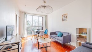 A modern living room with a sofa, a dining table with chairs, a TV, and a large window. - Beautiful flat 2 rooms near Paris/La Défense (Suresnes)