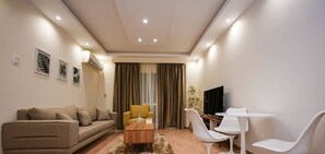 Relax in this stylish living room with a beige sofa, armchair, and dining table, perfect for unwinding with a flat-screen TV and a view.