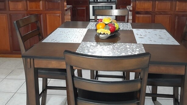Une cuisine avec des meubles de rangement en bois, une cuisinière et un réfrigérateur. On y trouve une table à manger avec des chaises et un panier de fruits posé dessus.
