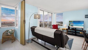 Una sala de estar moderna con un sofá, una butaca, un televisor y vistas a un paisaje urbano a través de amplios ventanales.
