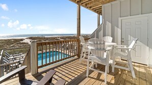 A wooden deck with a pool, white chairs, and a view of the beach. - Hypnautic East (Gulf Shores)