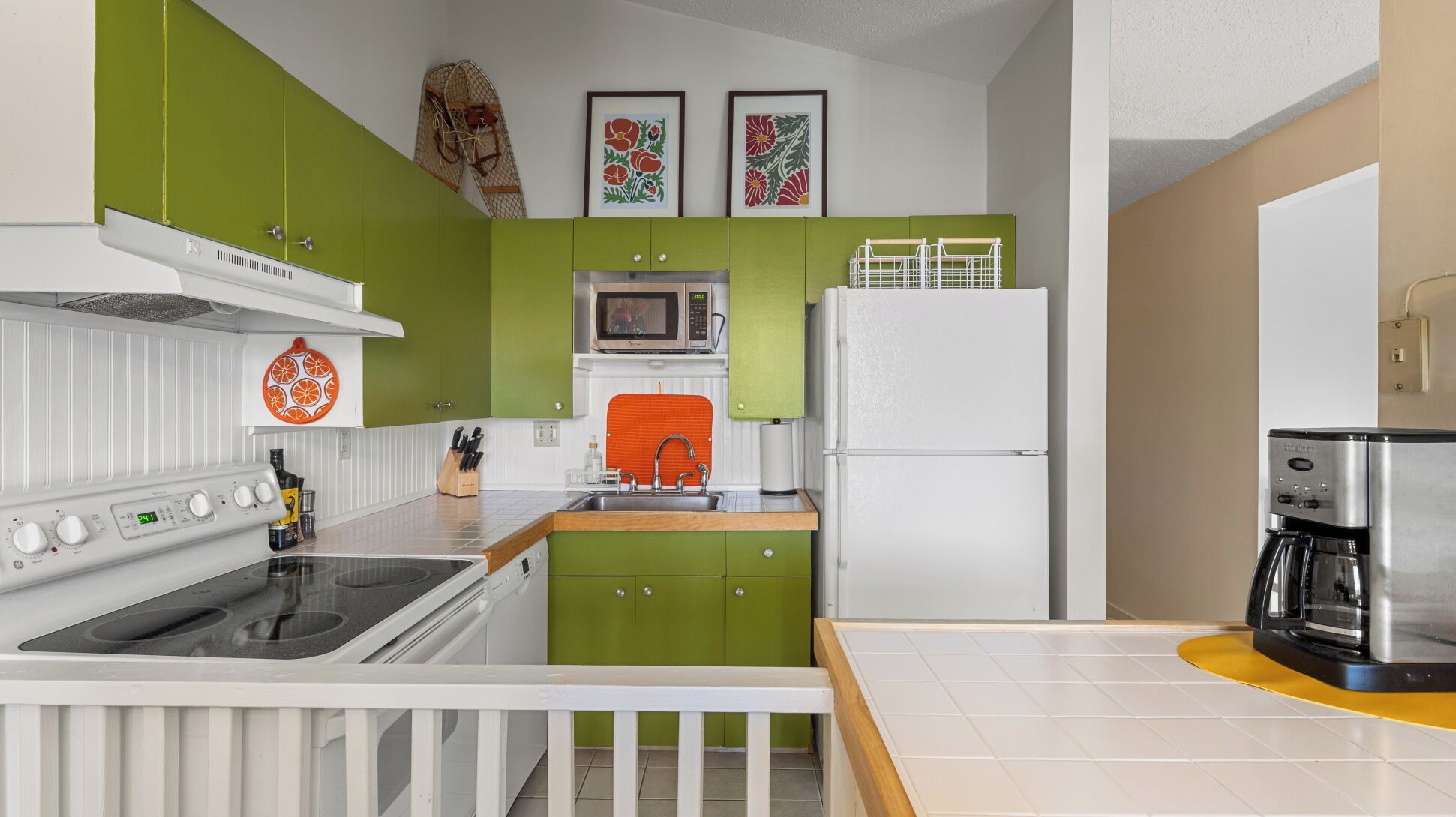A compact kitchen with green cabinets, a white refrigerator, a microwave, and a coffee machine.