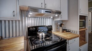 Una cucina compatta con un piano cottura in acciaio inossidabile, mobili bianchi e un piano di lavoro in legno.