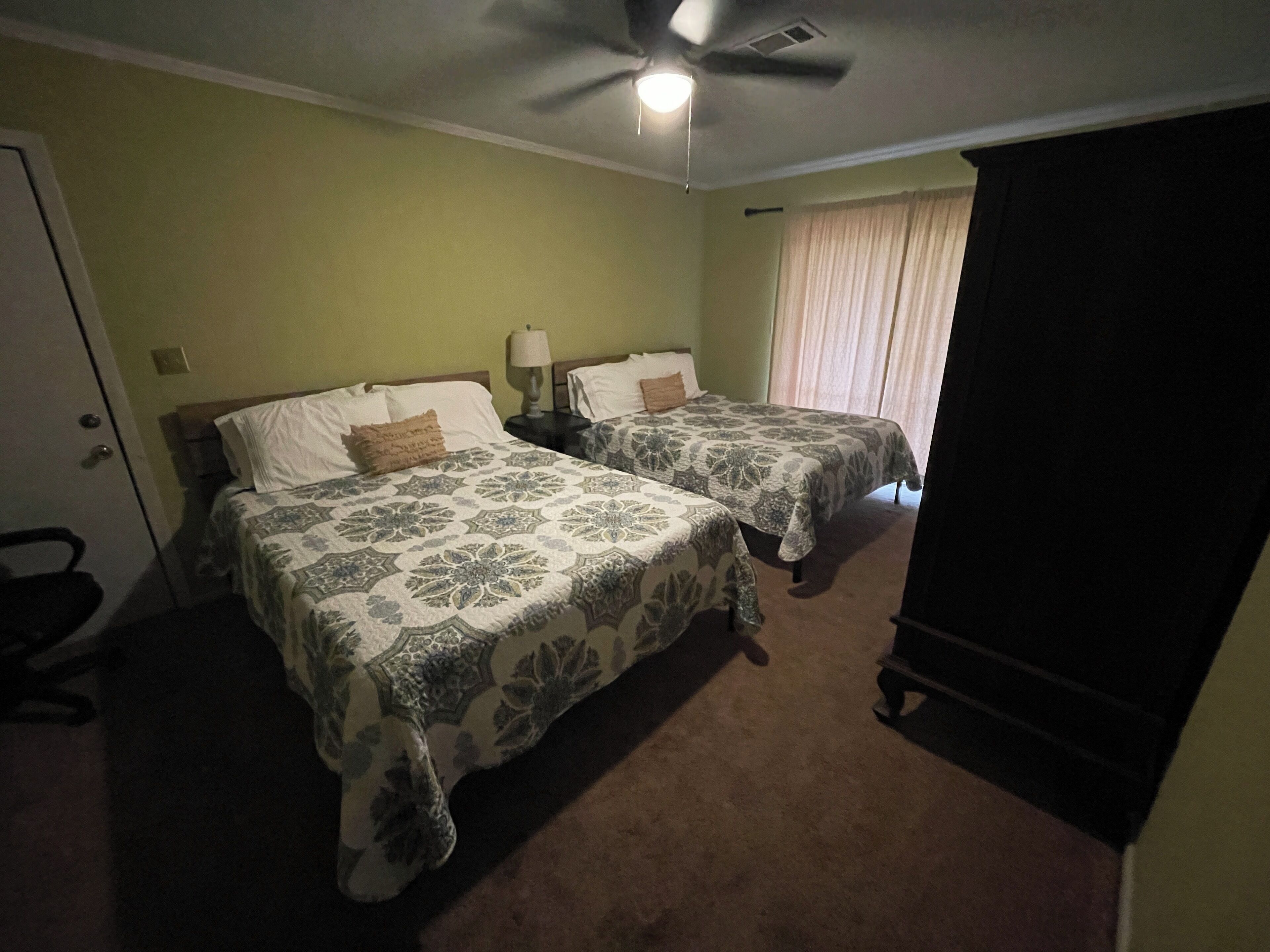 A room with two beds, a ceiling fan, a door, and a window with curtains.