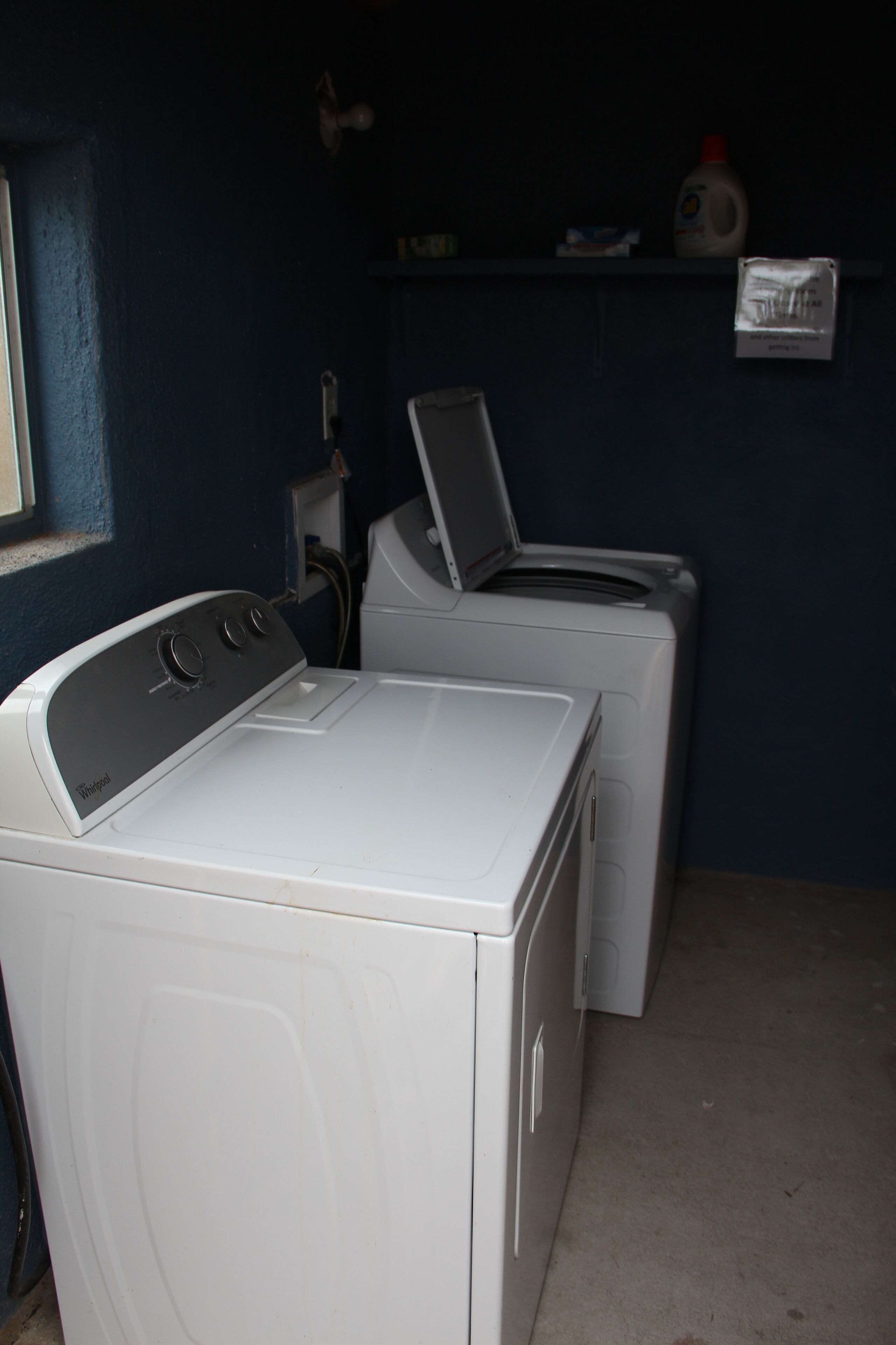 Une buanderie équipée de deux machines à laver à chargement frontal et d’une étagère contenant des produits de lessive.