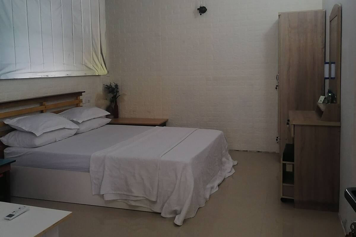 A bedroom with a bed, a nightstand, a desk, a wardrobe, and a ceiling fan.