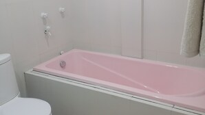 Et badeværelse med et hvidt toilet, et pink badekar og en brusehoved.