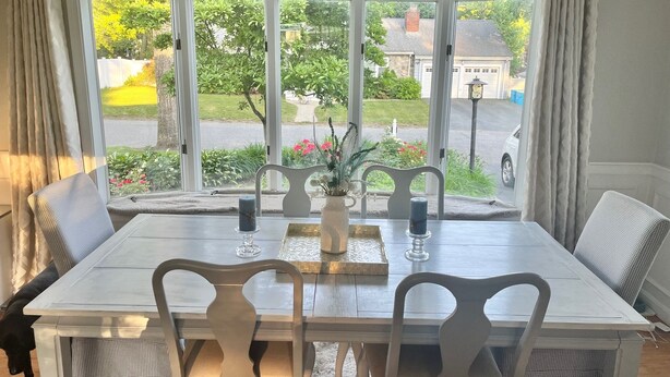 A dining table with white chairs and a vase with flowers.