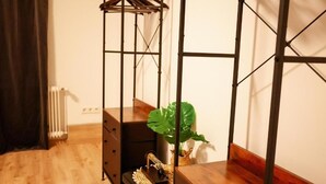 Una habitación con suelo de madera, un radiador, un aparador negro, un perchero de madera y una planta en maceta.