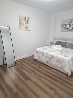 A bedroom with a bed, a bedside table, a mirror, and two wall art pieces. - MODERN AND NEW APARTMENT IN HUELVA (Huelva)