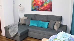 A grey sectional sofa with teal and grey cushions, a white floor lamp, and a colorful abstract painting on the wall. - MODERN AND NEW APARTMENT HUELVA (Huelva)