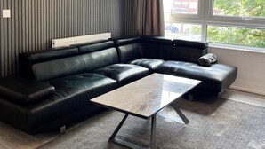 A modern living room with a black leather sectional sofa, a glass coffee table, and a yellow pendant light.