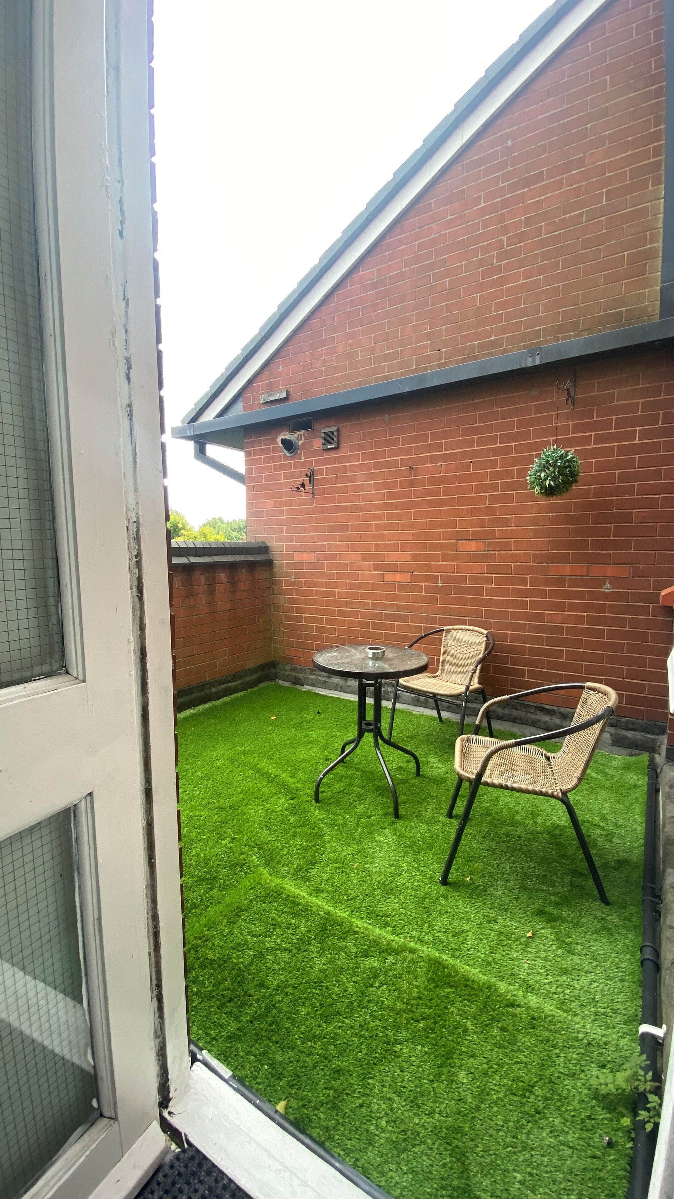 A patio with artificial grass, a table, and two wicker chairs.