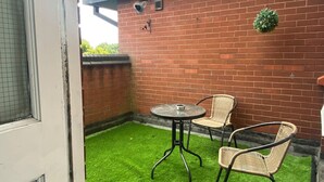 A patio with artificial grass, a table, and two wicker chairs.