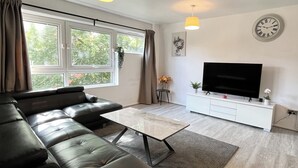 A modern living room with a leather sofa, a flat-screen TV, and a large window with curtains.