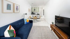 A modern living room with a dark blue sofa, a flat-screen TV, and framed artwork on the wall. - Beautiful Studio with Patio in Midtown NYC! #202 (New York)