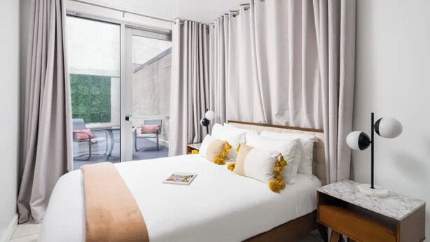 A bedroom with a large bed, a nightstand, and a view of an outdoor area. - Beautiful Studio with Patio in Midtown NYC! #202 (New York)
