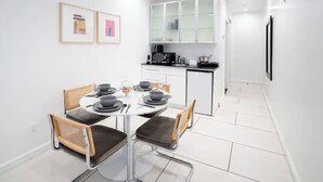 A modern kitchen with white cabinets, a dining table set for four, and two framed pictures on the wall. - Beautiful Studio with Patio in Midtown NYC! #202 (New York)