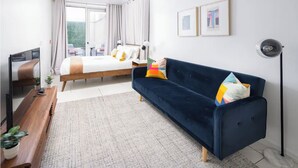 A modern hotel room with a bed, a dark blue sofa, a TV, and a desk with a plant. - Beautiful Studio with Patio in Midtown NYC! #202 (New York)